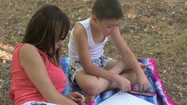 Mother draws from a six year old son. Mother with her son are drawing pictures in the park