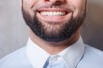 Perfect beard. Close-up of young bearded smiling man standing against grey background