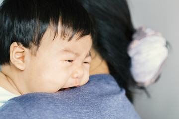Adorable baby girl cry on mom shoulder.