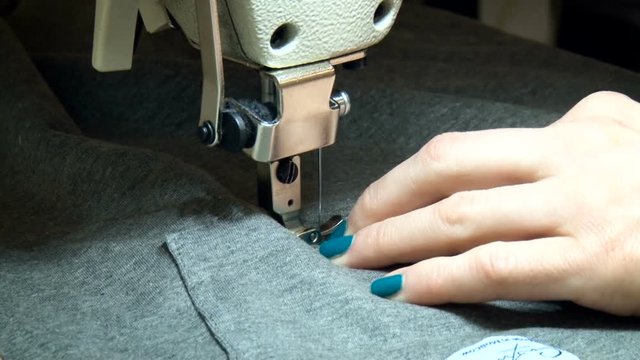 Female Seamer Working on Sewing Machine. Seamstress Stitching, Rotating Dress Parts. Well Groomed Hands With Manicure. Grey Fabric.neat Work Closeup