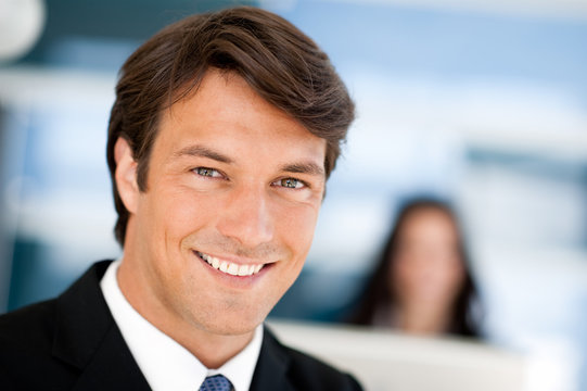 Smiling male supervisor boss businessman close-up in office with businesswoman blurred in background