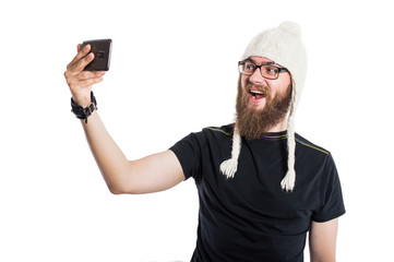 Joyful man with a beard in a funny hat and sunglasses. It makes selfie phone. On white, isolated background.