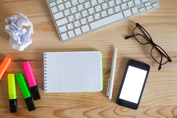 office supplies on the wooden table, notepad with place for text and smartphone with blank screen