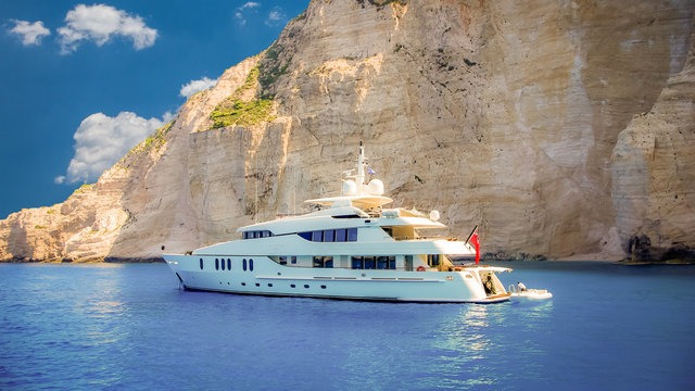 Fototapeta Luxury white yacht navigates into beautiful blue water near Zakynthos island. View from the top of a large white yacht at Navagio Beach.