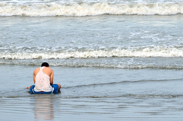 A dad and his boy sitting on the shore of the beach.