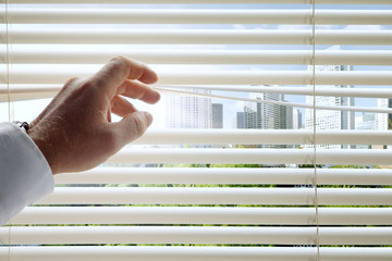 close up view of man's head spreading blinds and sunny city  background 