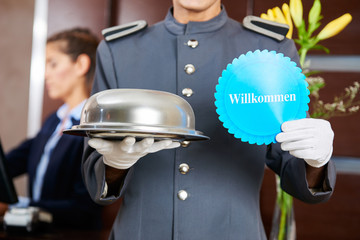Hoteldiener hält Speiseglocke und Willkommen Schild