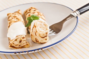 thin crepes rolled pancakes with sour cream mint on a plate