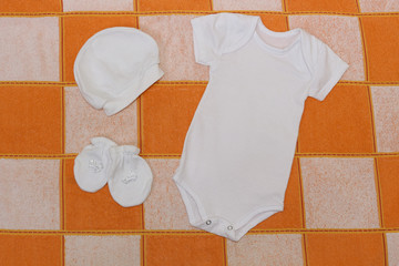 Things for babies in orange and white checkered blanket . White bodysuit , white cap , white...