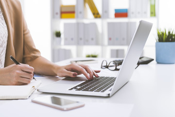 Close up of girl in beige cardigan writing and typing