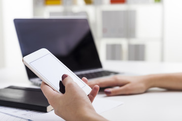 Woman's hand with smartphone. Laptop at background