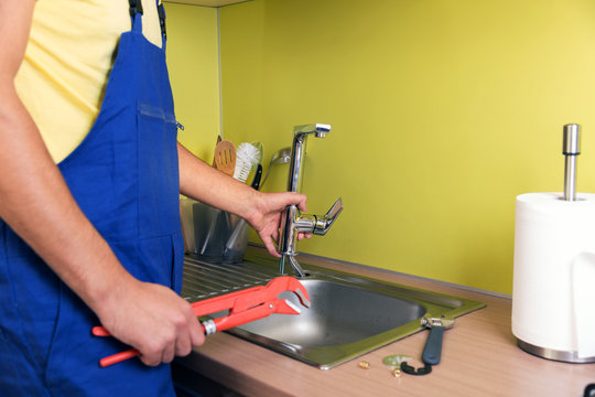 plumber working in domestic kitchen, repairing faucet