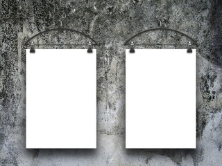 Two blank frames hanged by clothes hangers against dark dirty gray concrete wall background