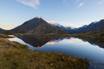 Naklejka na ściany i meble High altitude alpine lake in idyllic land with reflection of majestic rocky mountain peaks glowing at sunset. Wide angle view on the Alps.