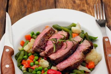 Sliced Beef steak medium rare with asparagus beans,cauliflower,carrot and pea on wooden table.closeup selective focus.Fork and knife