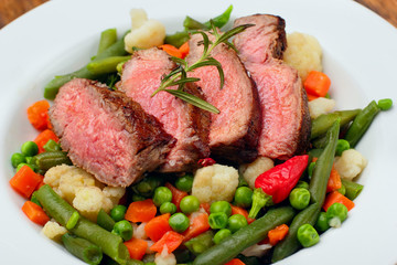Sliced Beef steak mediu, rare with asparagus beans,cauliflower,carrot and pea on wooden table.closeup selective focus