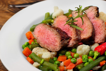 Sliced Beef steak mediu, rare with asparagus beans,cauliflower,carrot and pea on wooden table.closeup selective focus