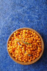 buckthorn in a wooden bowl on blue background