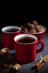 Red cups with tea on gray concrete background, cinnamon and walnuts