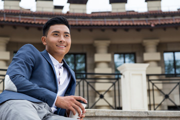 Cheerful Asian man with cup of coffee