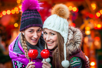 Frauen trinken Glühwein und essen Zuckerstangen auf deutschen Weihnachtsmarkt