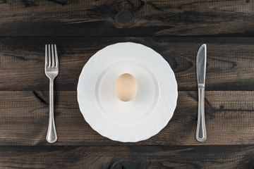 egg on white plate with fork and butter knife on wooden table