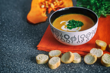 Cream pumpkin soup with fresh herbs and crackers on dark stone background. Healthy food. Selective focus.
