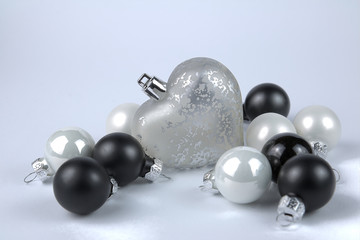 weißes Glasherz umgeben von matten, glänzenden schwarzen und weißen Christbaumkugeln