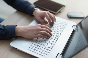 Hands typing on a laptop keyboard. A man works in an office at his workplace