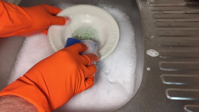 Мужчина моет посуду. Видны руки, тарелки, мойка