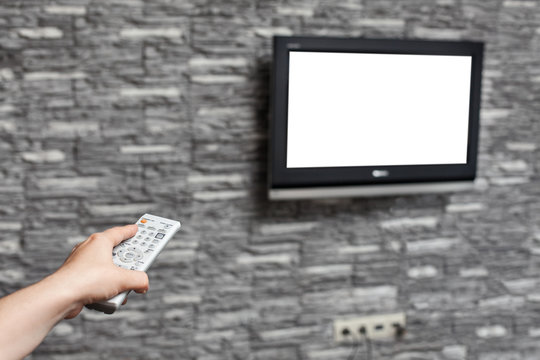 Human hand pushing tv remote control, tvset with white isolated screen hanging on wall