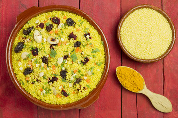 Vegetable couscous in a clay pot, with raw couscous and a spoon with turmeric