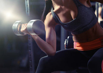 Fototapeta na wymiar Young woman flexing muscles with dumbbell in gym