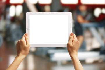 Female hands holding tablet on blurred gym background