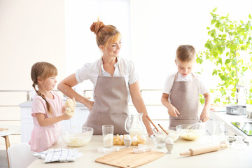 Young mother and kids making dough in kitchen