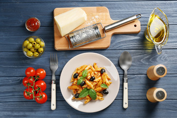 Delicious penne pasta with ingredients on wooden table