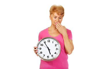 Elderly yawning woman holding big clock