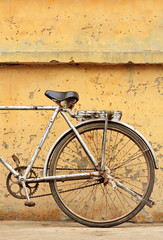 Fototapeta na wymiar Rusty Chinese bike against weathered yellow wall