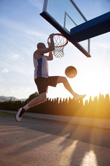 Young man jumping and making a fantastic slam dunk playing stree
