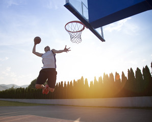 Young man jumping and making a fantastic slam dunk playing stree
