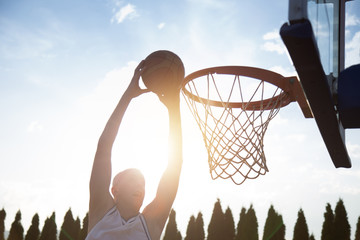 Young man jumping and making a fantastic slam dunk playing stree