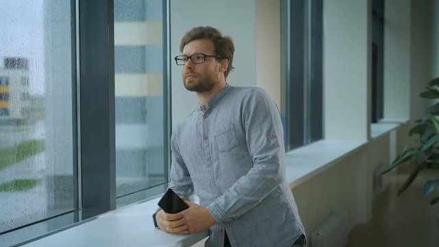 A man standing in corridor holding and looking out the window.