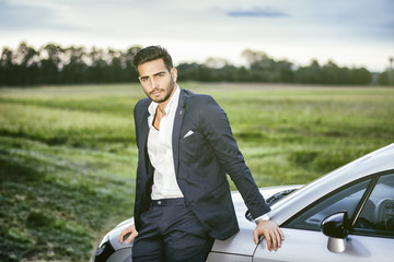 Portrait of young attractiave man in business suit sitting in his new stylish car outdoor in...