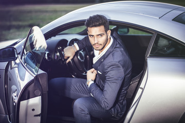 Portrait of young attractiave man in business suit sitting in his new stylish car outdoor in...
