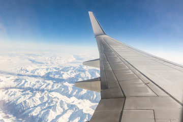 Airplane window seat view while flying over snowy mountains