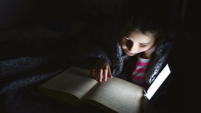 girl teen child reads book reading night with flashlight lying a under blanket