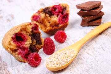 Muffins with raspberries, chocolate and oat bran on spoon, wooden background, delicious dessert