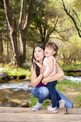 Naklejka premium Asian Woman with her little daughter in the woods near the river standing on a log