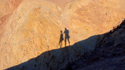 Two shadows of hikers silhouettes on a background of yellow mountains