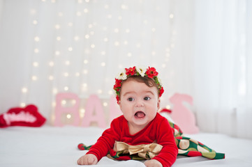 Fototapeta premium Cute little baby girl with wreath and on red dress posed on the